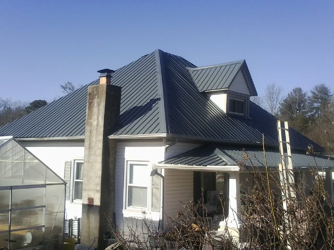 Dark blue standing seam metal roof on a white farmhouse with dormer — Slate & Tile Roof Repair by Roofing Brothers in Apple Creek