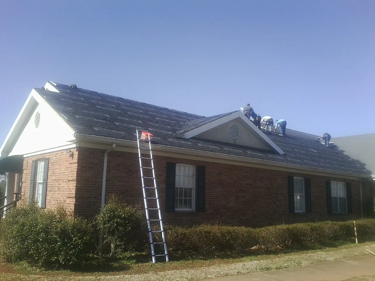 Crew tearing shingles off a brick ranch roof with a ladder set — Emergency Roof Repair work by our crew in Apple Creek
