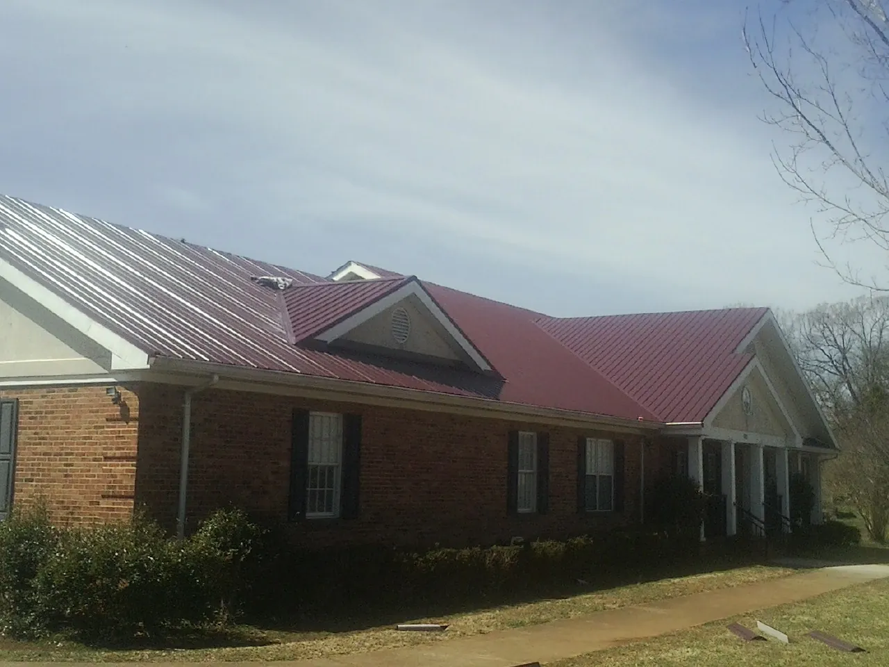 Red metal roof with gabled entries on a long brick building, from a Hail Damage Roof Repair job in Apple Creek