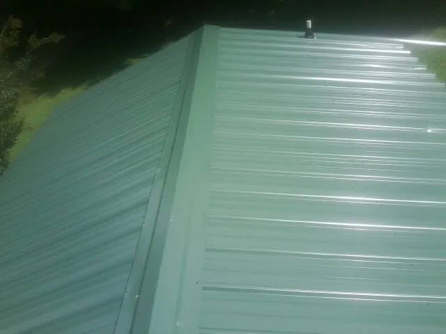 New green metal panels meeting at the ridge of a roof — Flat Roof Repair work by our crew in Apple Creek