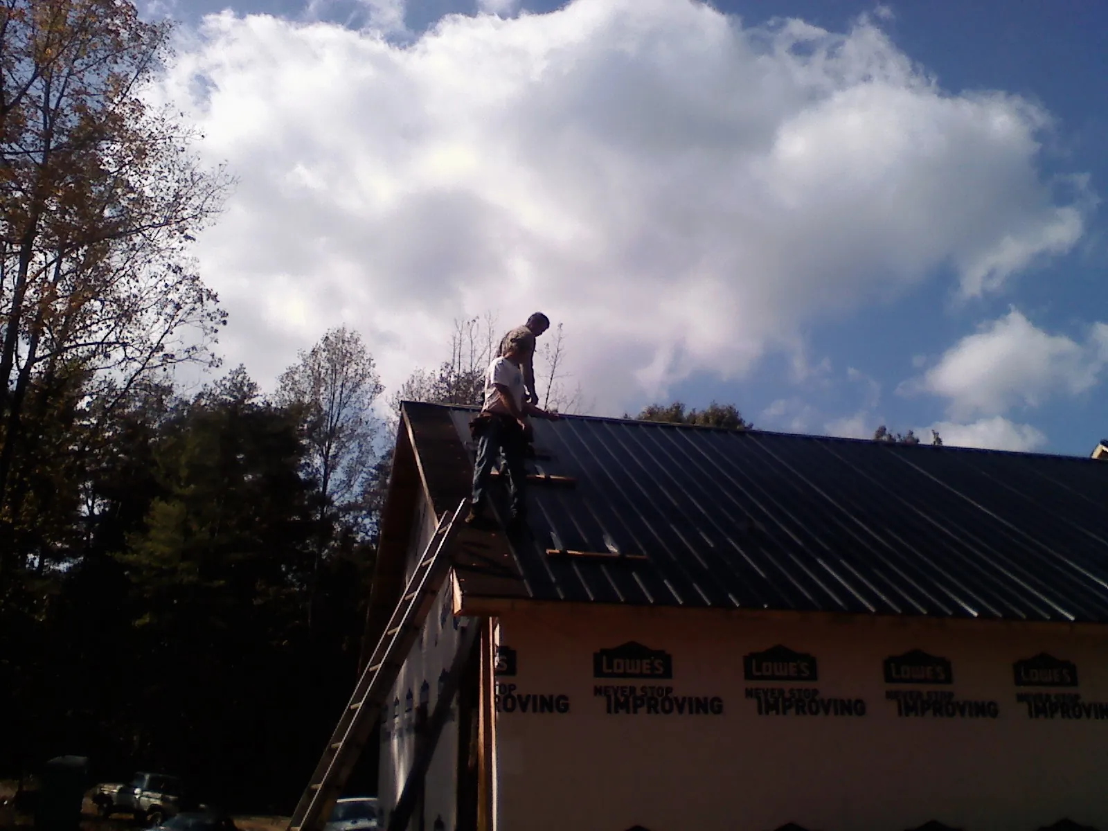 Roofer fastening dark metal panels high against a cloudy sky, from a Roof Inspection job in Apple Creek
