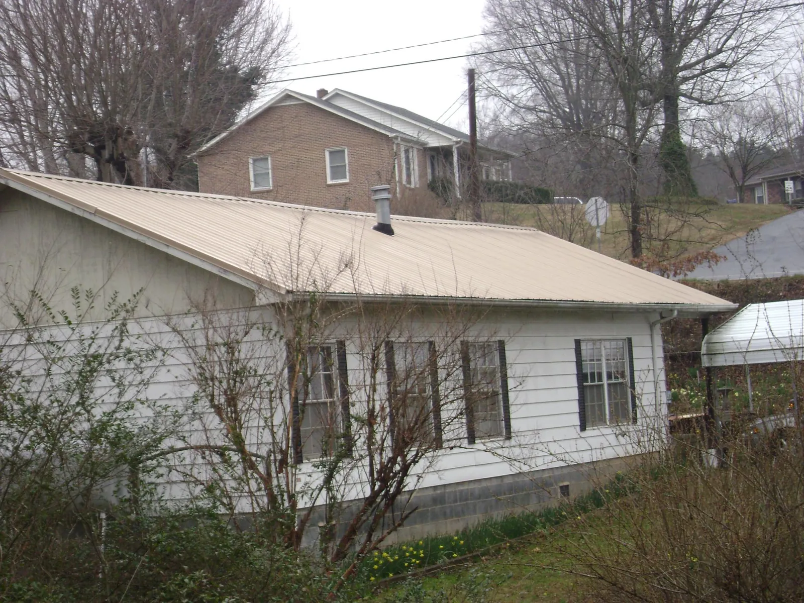 Tan metal roof on a white sided house set into a hillside — Commercial Roofing by Roofing Brothers in Apple Creek