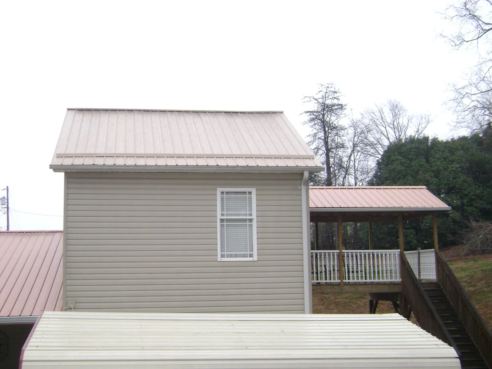 Tan metal roofs on a two story addition and attached porch, from a Roof Replacement job in Apple Creek
